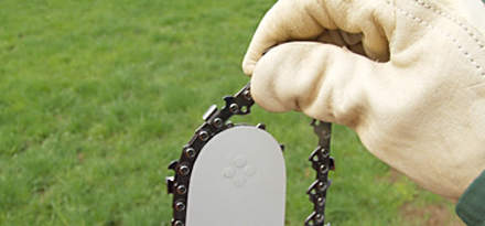: Step 4 of 14: Always wear gloves when working on the chain because of the high risk of injury from the sharp teeth. Start by picking up the chain and guide bar and route the chain around the guide bar, starting at the bar nose. Make sure that the chain is running in the correct direction => (refer to picture).