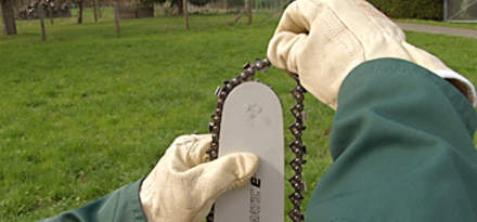 : Step 4 of 15: Always wear gloves when working on the chain because of the high risk of injury from the sharp teeth. Start by picking up the chain and guide bar and route the chain around the guide bar, starting at the bar nose. Make sure that the chain is running in the correct direction => (refer to picture).